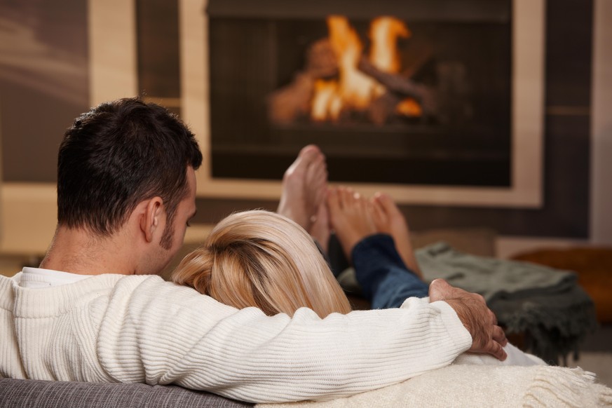 Young couple hugging on sofa in front of fireplace at home, rear view. Click here for more &quot;People at Home&quot; images: