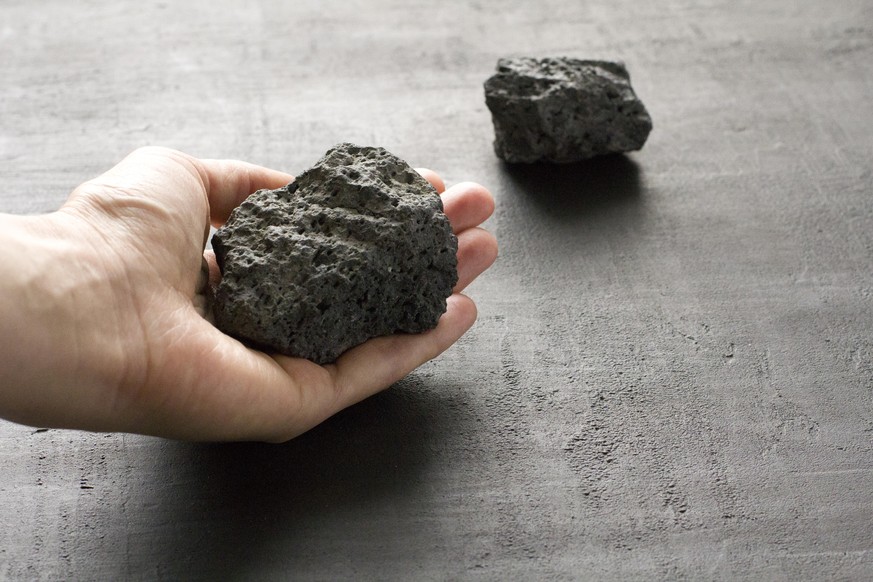 Female hand holds a black stone of lava and magma from the volcano Etna on the island of Sicily, Italy. Stone after the eruption of volcano. Natural black stone, mineral on black background, close-up.