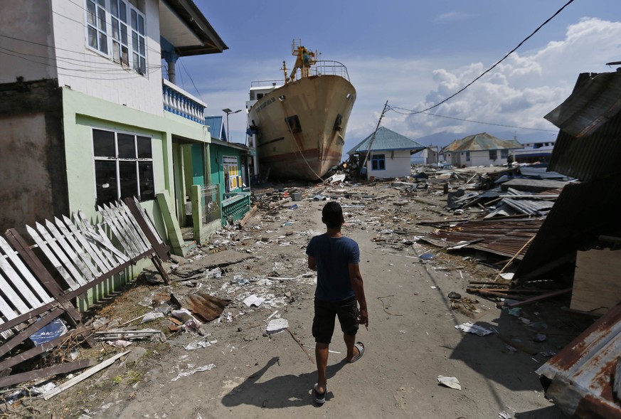 In this Thursday, Oct. 4, 2018, photo, a man walks past the Sabuk Nusantara 39 ship which was swept ashore by the tsunami in Wani village on the outskirt of Palu, Central Sulawesi, Indonesia Indonesia ...
