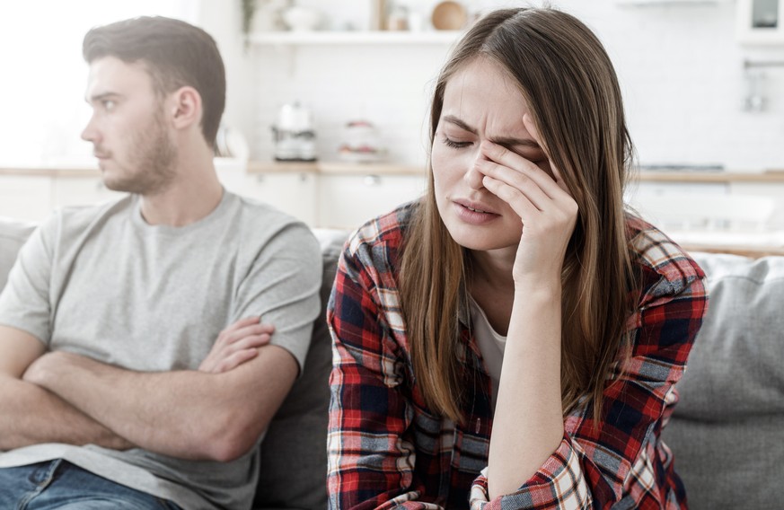 Couple conflict. Stressed crying female sitting on couch with abusive husband after quarrel, ready to divorce