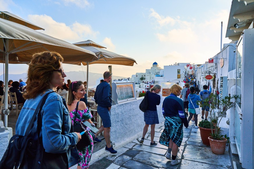 Tourists in restaurants and on Oia Castle wait for the sunset with Caldera View and the famous Windmill in Oia, Santorini , Greece at 04 June 2019. Photographer: Peter Schatz