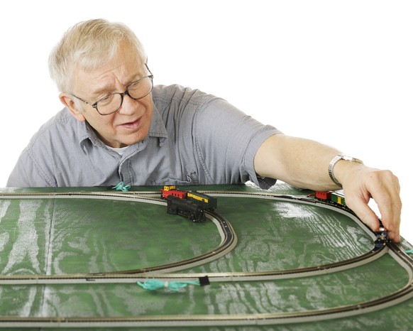 A senior man placing an engine on the track as he sets up a new N-Guage train set. Focus is on the man. On a white background.