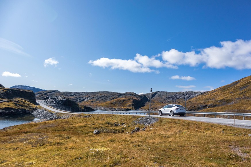 Myrkdalen, Norway - September 08, 2019: White Tesla X electric car driving Norway highway mountain road on sunny bright day