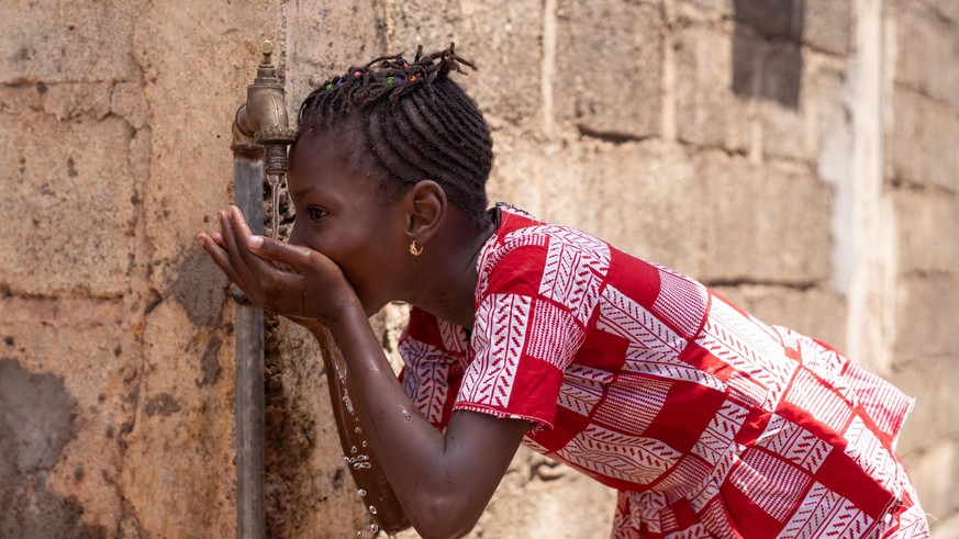 Little Black Girl Drinks Water Outdoors. Candid Picture of African children drinking and playing with water in Bamako, Mali.