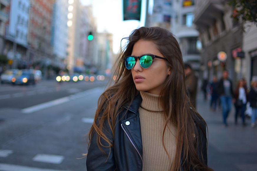 urban young girl walking on the Gran Via street in Madrid during sunset wearing sunglasses and black jacket