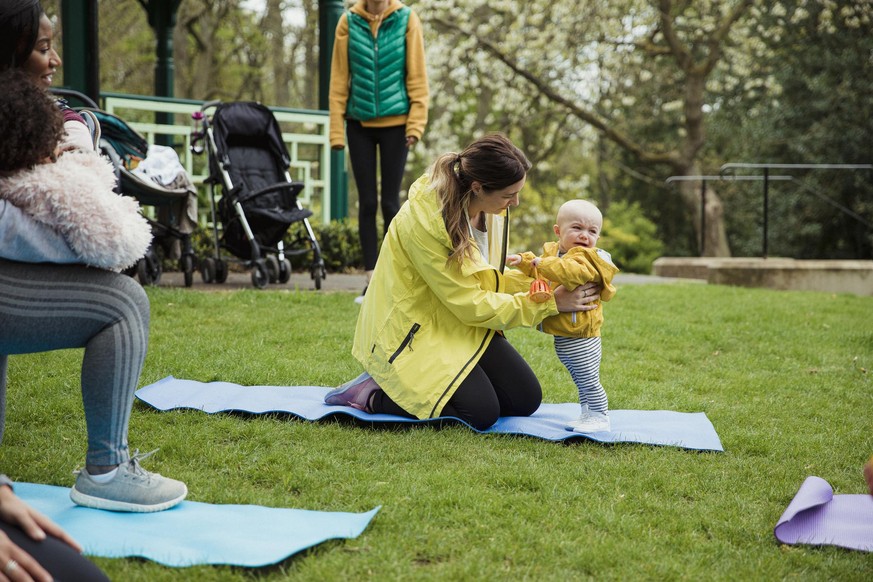 A mother is attending an exercise class in the park whereby her and her cute son are doing yoga.