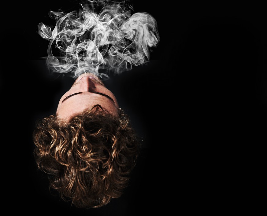 Top view a young man blowing out smoke against a black background