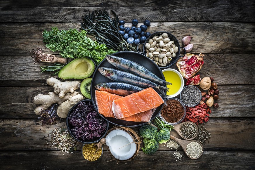 Top view of healthy, antioxidant group of food placed at the center of a rustic wooden table. The composition includes food rich in antioxidants considered as a super-food like avocado, kale, blueberr ...