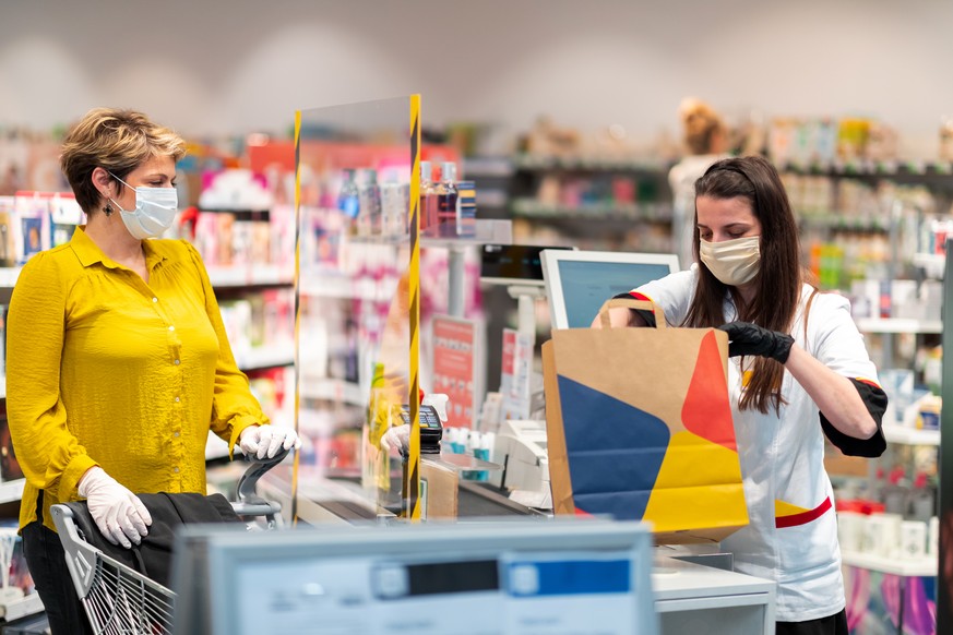 Female customer wearing protective face mask and protective gloves to prevent Corona virus and other diseases, sales clerk packing disinfection items, also wearing protective mask and gloves, Covid-19 ...