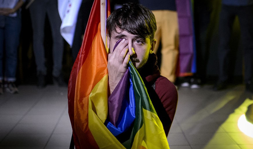 A man sits draped in a rainbow flag in a nightclub in Bucharest, Romania, Sunday, Oct. 7, 2018, after hearing of the partial voter turnout. Polls have closed in Romania after two days of voting on a c ...