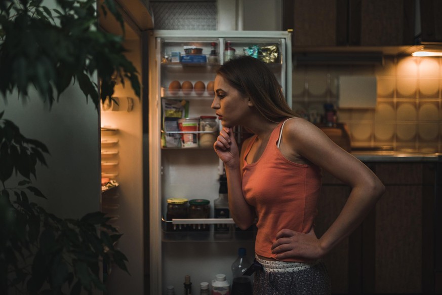 Young woman wearing pajamas looking for a snack in the refrigerator late night