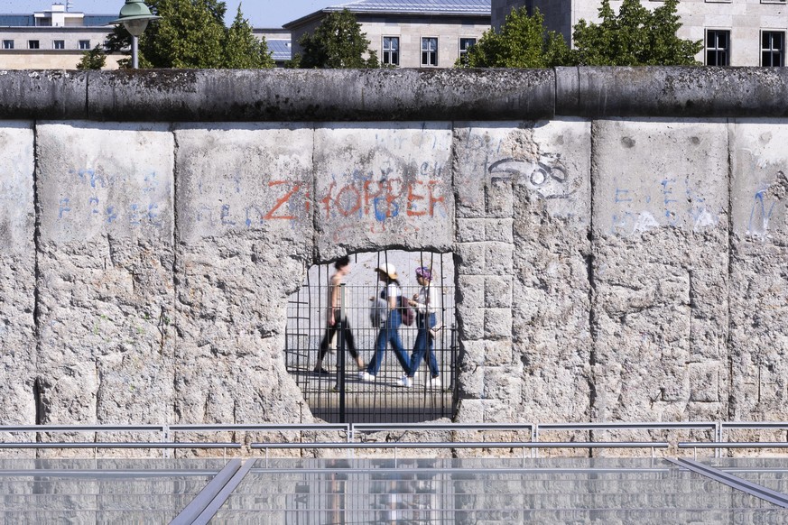 11.08.2020, Berlin: Passanten sind durch ein Loch in einem verbliebenem Stück der Berliner Mauer an der Niederkirchnerstraße zu sehen. Vor 59 Jahren, am 13. August 1961, begann der Bau der Mauer, die  ...