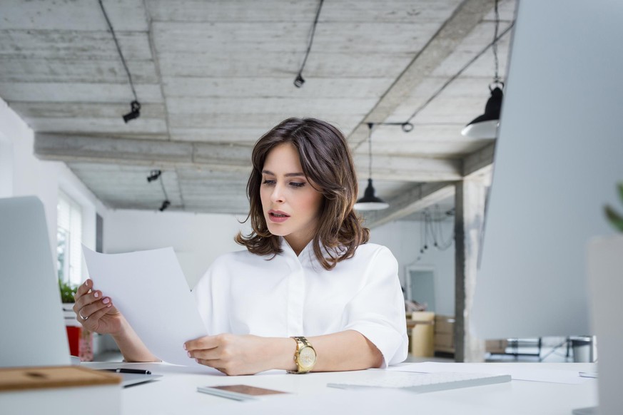 Worried businesswoman reading a document while sitting at her desk in office. Female executive reading a paper seriously.