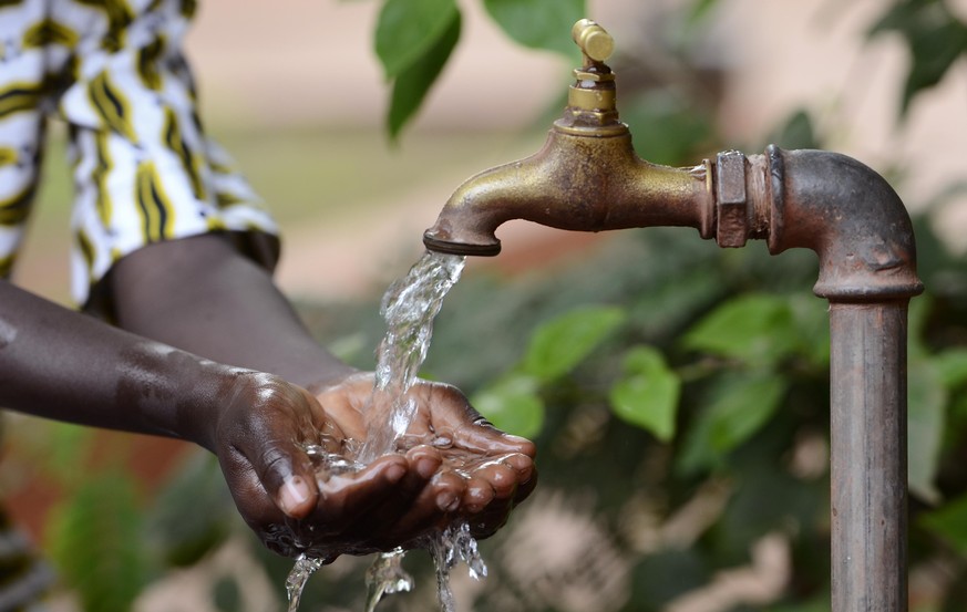 Hand of an African black boy with water pouring from a tap. Water scarcity or lack of safe drinking water is one of the world&#039;s leading problems affecting more than 1 billion people globally, mea ...