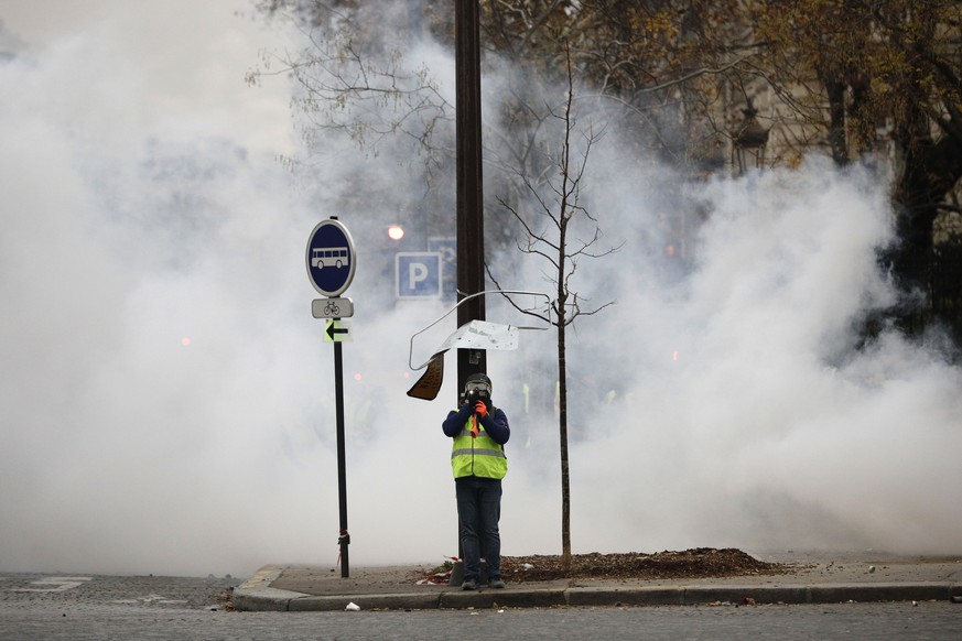 A demonstrator uses his phone amid tear gas near the Champs-Elysees avenue during a demonstration Saturday, Dec.1, 2018 in Paris. French authorities have deployed thousands of police on Paris&#039; Ch ...