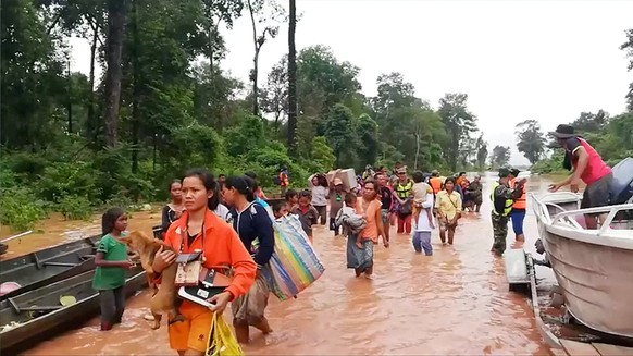 People walk through flooded area after being brought to safety by boat in Sanam Xay district, Attapeu Province, Laos after a hydropower dam under construction in Southern Laos collapsed, in this still ...