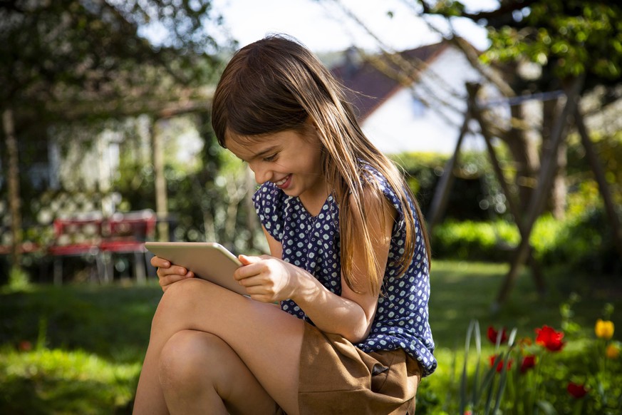 Happy girl sitting in garden using digital tablet model released Symbolfoto property released LVF08861