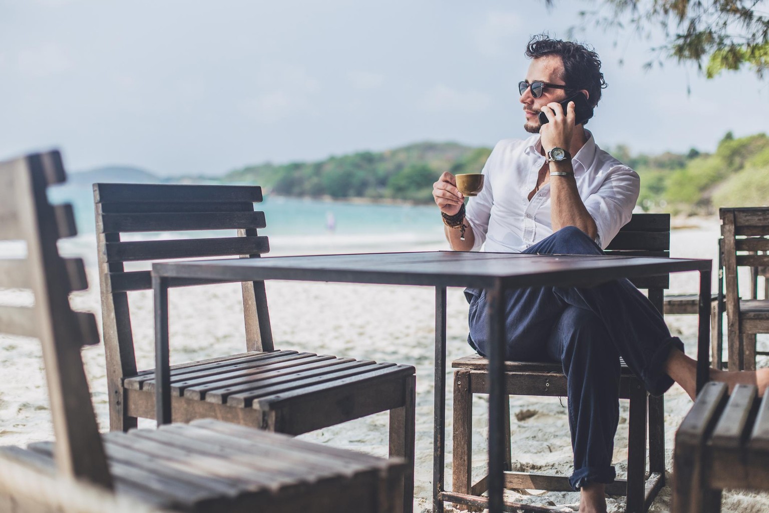 One man, man on the beach, drinking coffee in cafe, talking on mobile phone.