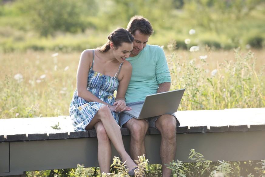 Couple sitting on countryside boardwalk with laptop computer PUBLICATIONxINxGERxSUIxAUTxONLY Copyright: EricxAudras B04659129
